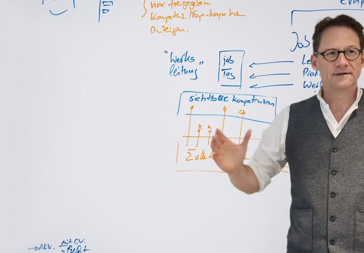 Deutsche Interim AG CEO Tilo Ferrari stands in front of a whiteboard and explains something.