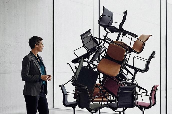 Kompetenz statt Festanstellung: Das Bild zeigt eine Frau vor einem Haufen aufgetürmter Stühle.