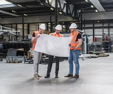 Interim Management Operations: The picture shows three men in work clothes in a production hall.