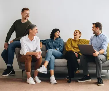 Interim Management Human Resources: This shows five people on a couch talking and laughing together.