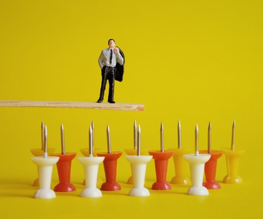 Wertschätzendes Trennungsmanagement: Das Bild zeigt eine Figur, die auf einem Eisstäbchen über Reißzwecken steht.