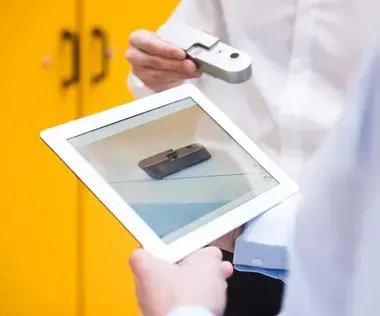 Interim Management: Das Bild zeigt zwei Kollegen, die sich auf einem Tablet über ein Gerät anaschauen.