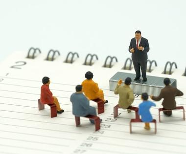 Talentmanagement: Das Bild zeigt die Figur eines Talentmanagers. Er steht auf einem Satz Tackernadeln vor Mitarbeitenden, die ebenfalls auf Tackernadeln sitzen.