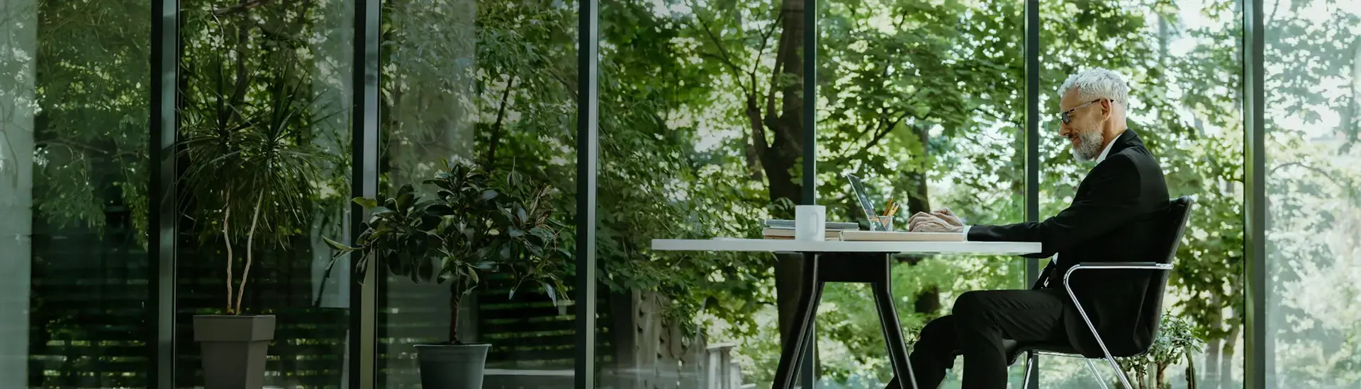 Interim Management CSR: The picture shows a working manager sitting in front of a glass front, behind which nature can be seen.