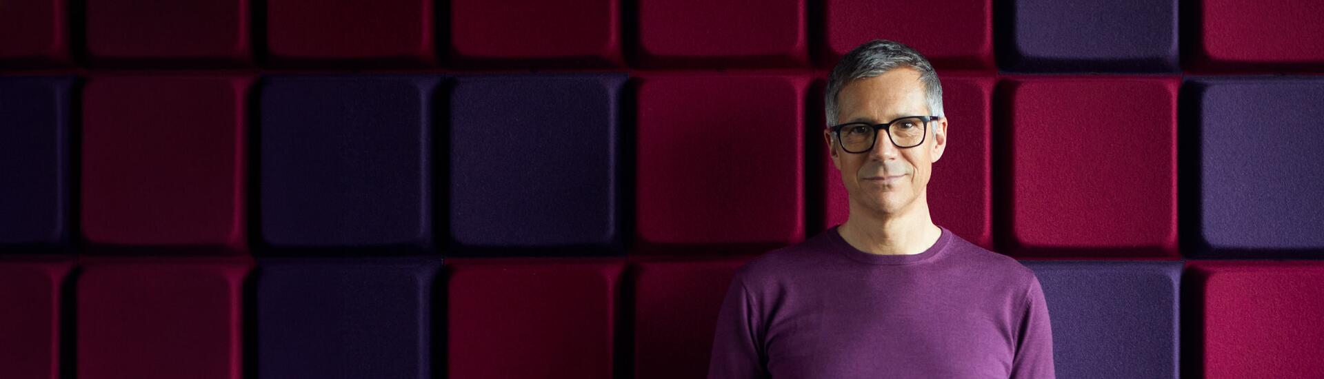 Interim Leiter IT: Das Bild zeigt einen IT-Leiter vor einer rot-lila-farbigen Wand.