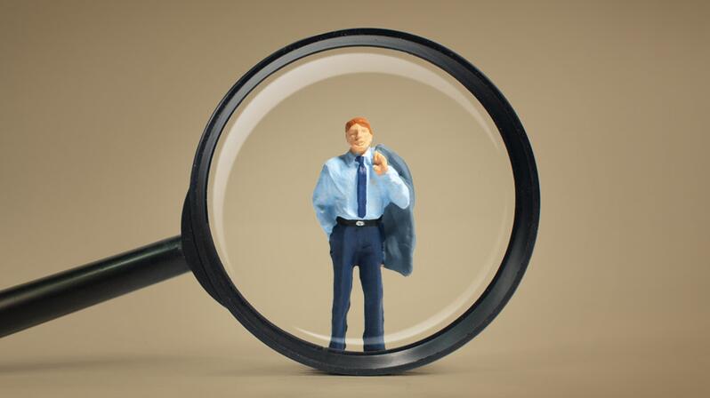 The picture shows a magnifying glass enlarging an interim manager.