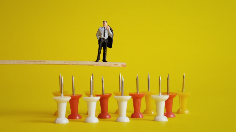 Wertschätzendes Trennungsmanagement: Das Bild zeigt eine Figur, die auf einem Eisstäbchen über Reißzwecken steht.