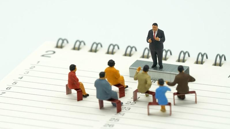 Talentmanagement: Das Bild zeigt die Figur eines Talentmanagers. Er steht auf einem Satz Tackernadeln vor Mitarbeitenden, die ebenfalls auf Tackernadeln sitzen.