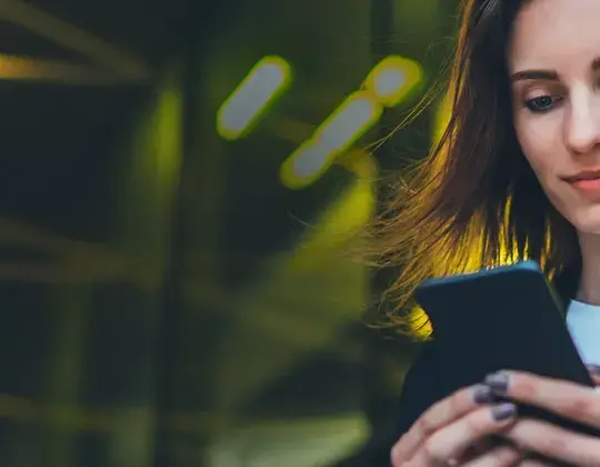 The picture shows a young woman looking at her smartphone.